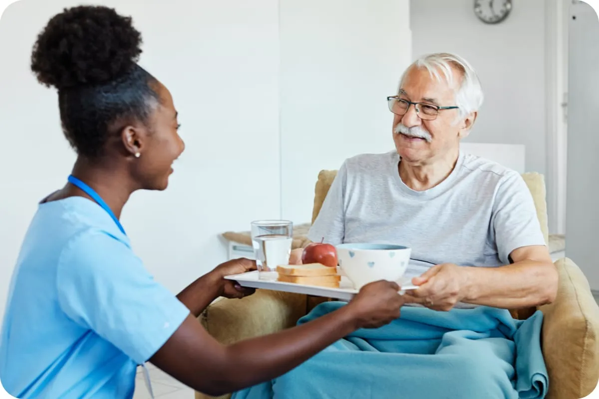 A caregiver bringing a tray to an older man at home