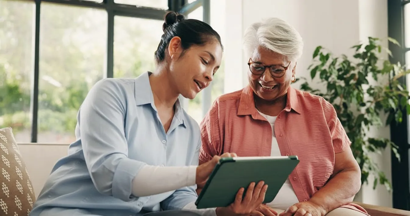 A caregiver and an older woman looking at a tablet together